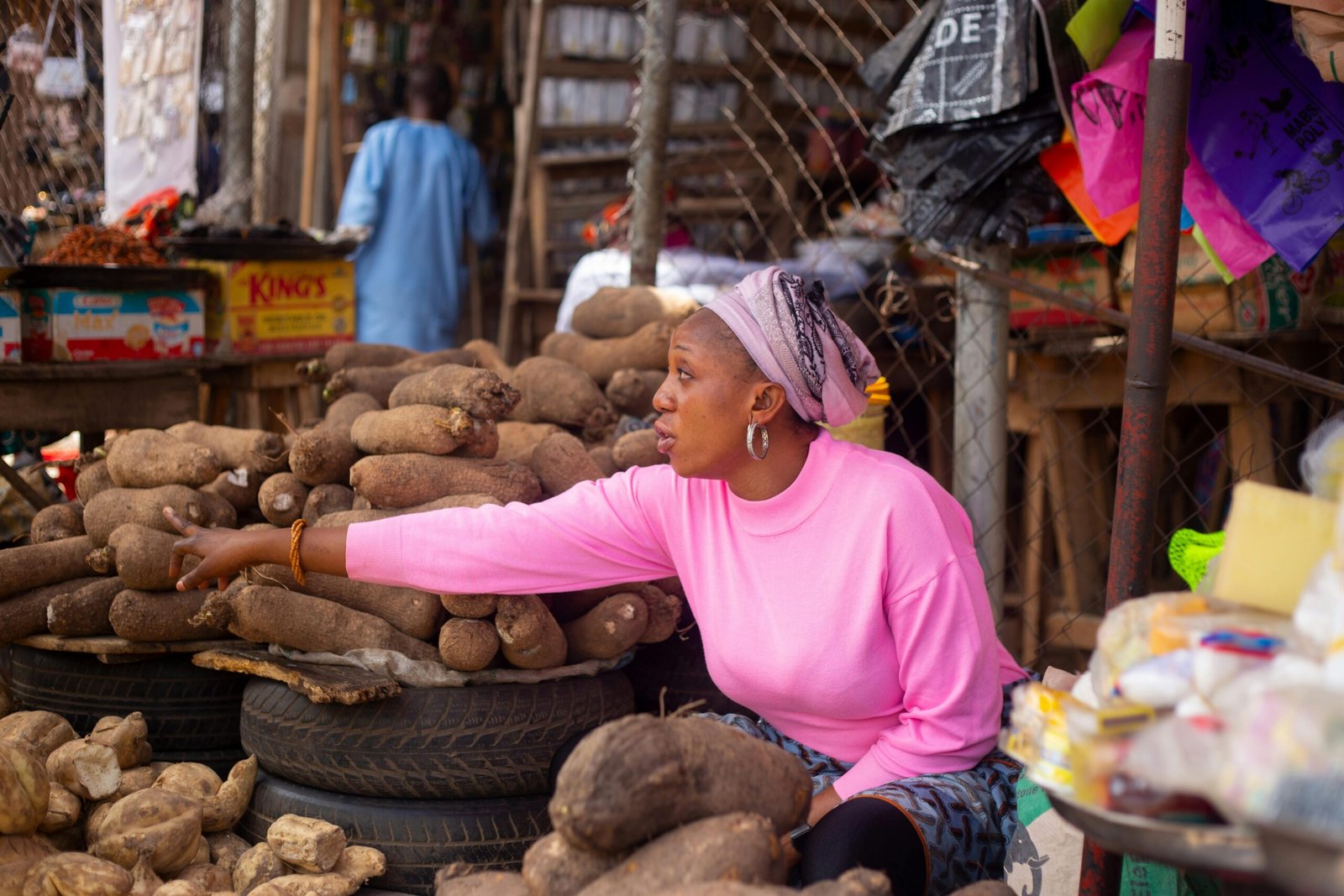 African woman vendor in a vibrant market selling yams, highlighting traditional commerce and culture.