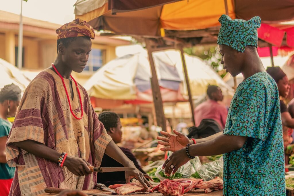 Two men in traditional African clothing interact at a vibrant outdoor market.